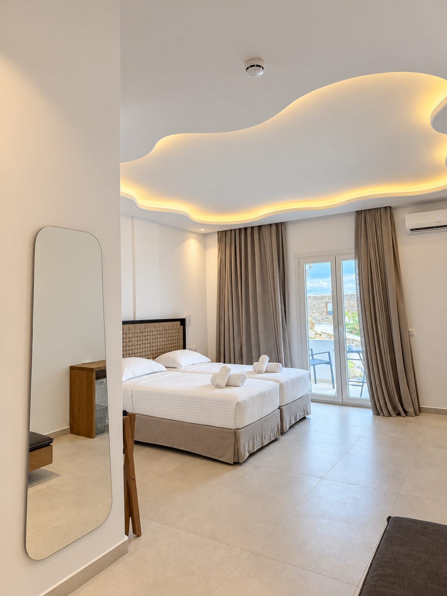 Suite with a rattan headboard, wavy lit ceiling and balcony door